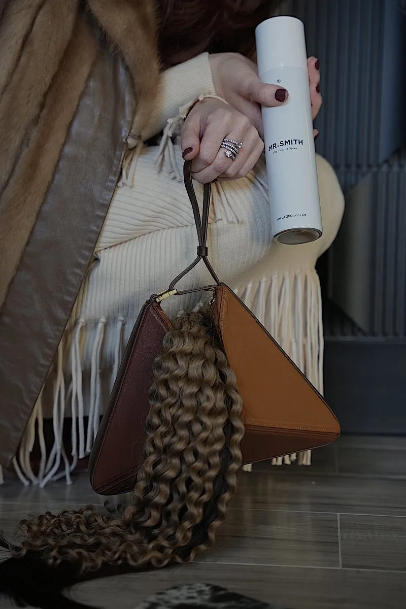 Curly hair resting over a bag next to a bottle of Mr. Smith styling spray