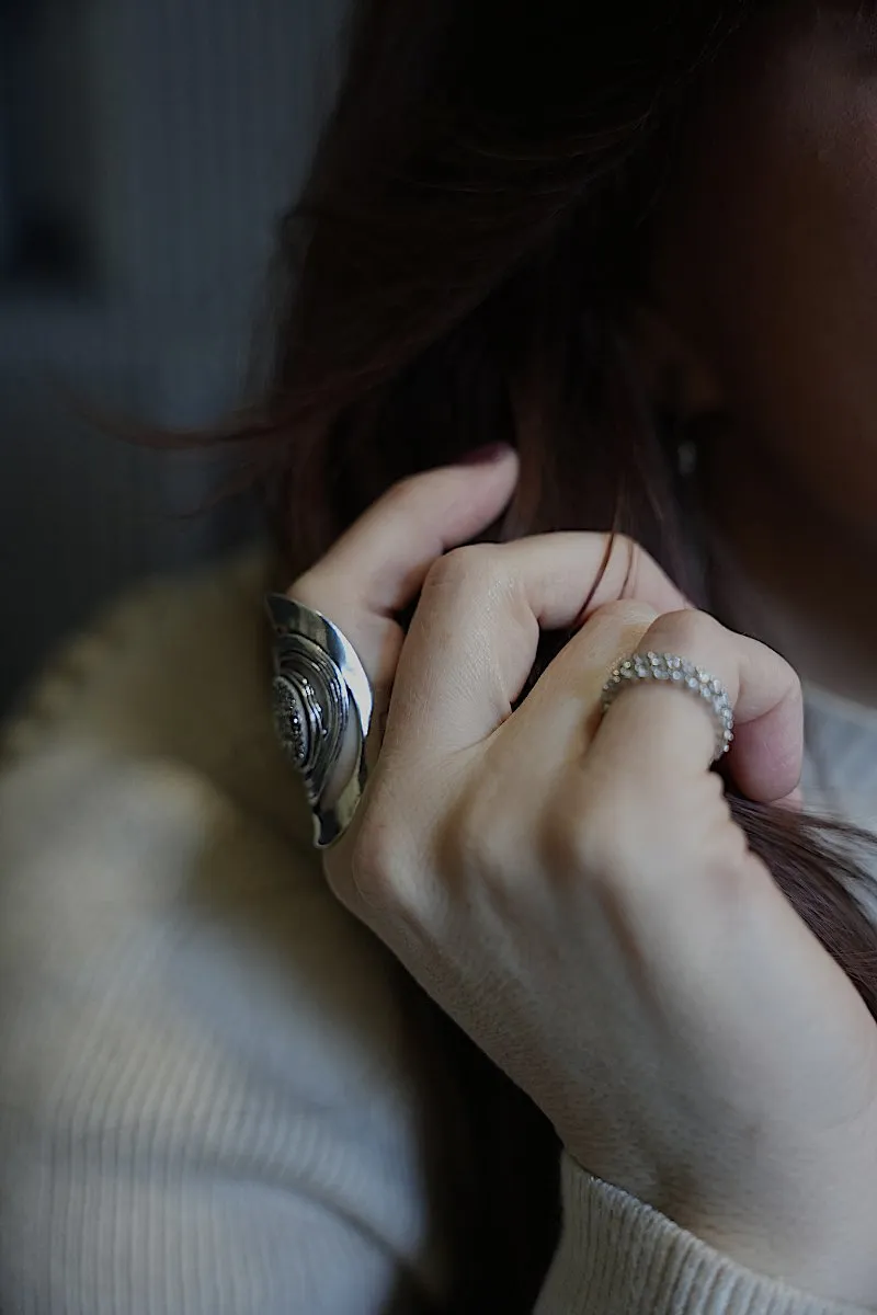 Close-up of a woman running her hand through her hair, wearing statement rings and a cream knit sweater
