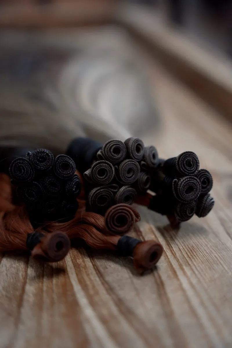 Close-up of hand-tied hair extension wefts resting on a wooden surface